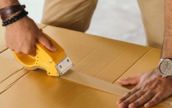 Persona pegando una caja de cartón con cinta adhesiva