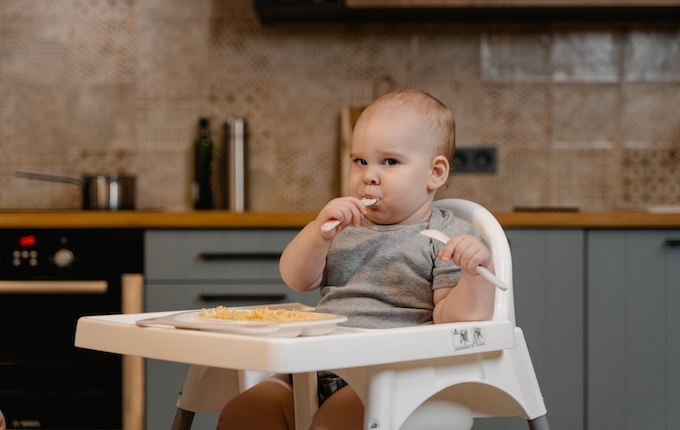 bébé mangeant avec une cuillère en silicone assis dans une chaise haute