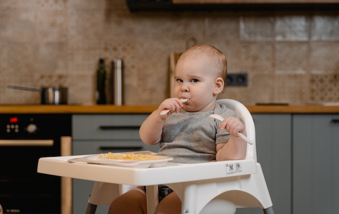 Baby isst mit einem Silikonlöffel im Hochstuhl