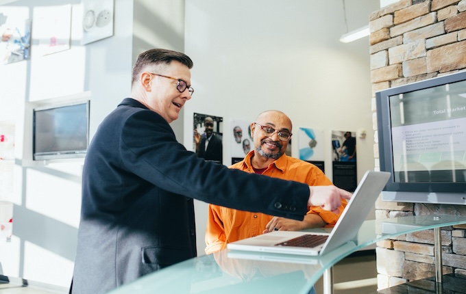Man helping someone with their business, pointing at a computer