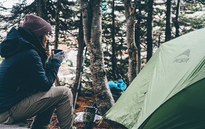 Woman sitting by a tent drinking coffee