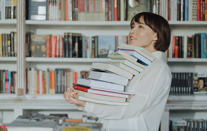Femme tenant une pile de livres dans une librairie